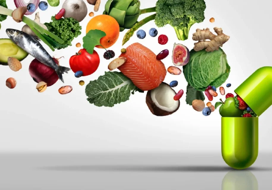 A green pill bottle filled with lots of fresh fruits and vegetables.