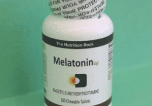 Melatonin dietary supplement bottle on green background.